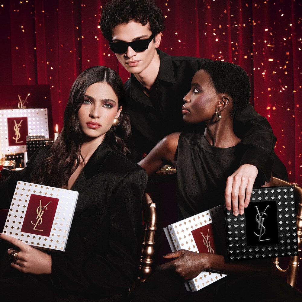 Models posing together holding luxury YSL Holiday gift boxes in a festive atmosphere.