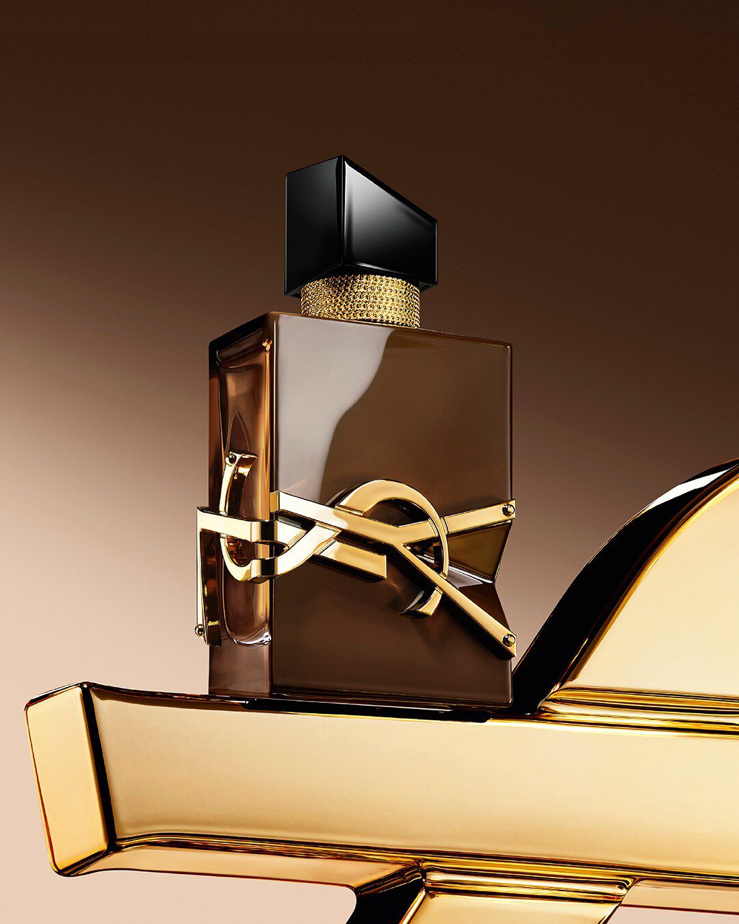 Glazed brown Libre Santal Couture bottle reflecting light, placed on a large golden YSL Cassandre.