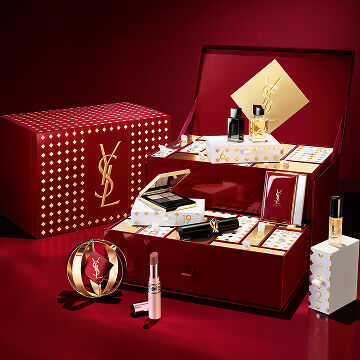 Assortment of luxury YSL Holiday gift sets elegantly displayed on a deep burgundy backdrop.