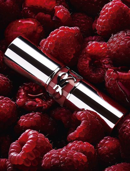 YSL LOVESHINE Berry Crush lipstick, silver tube with berry YSL logo, nestled among fresh raspberries.