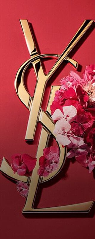 Gold YSL Cassandre logo adorned with vibrant pink spring flowers, set against a pink background.
