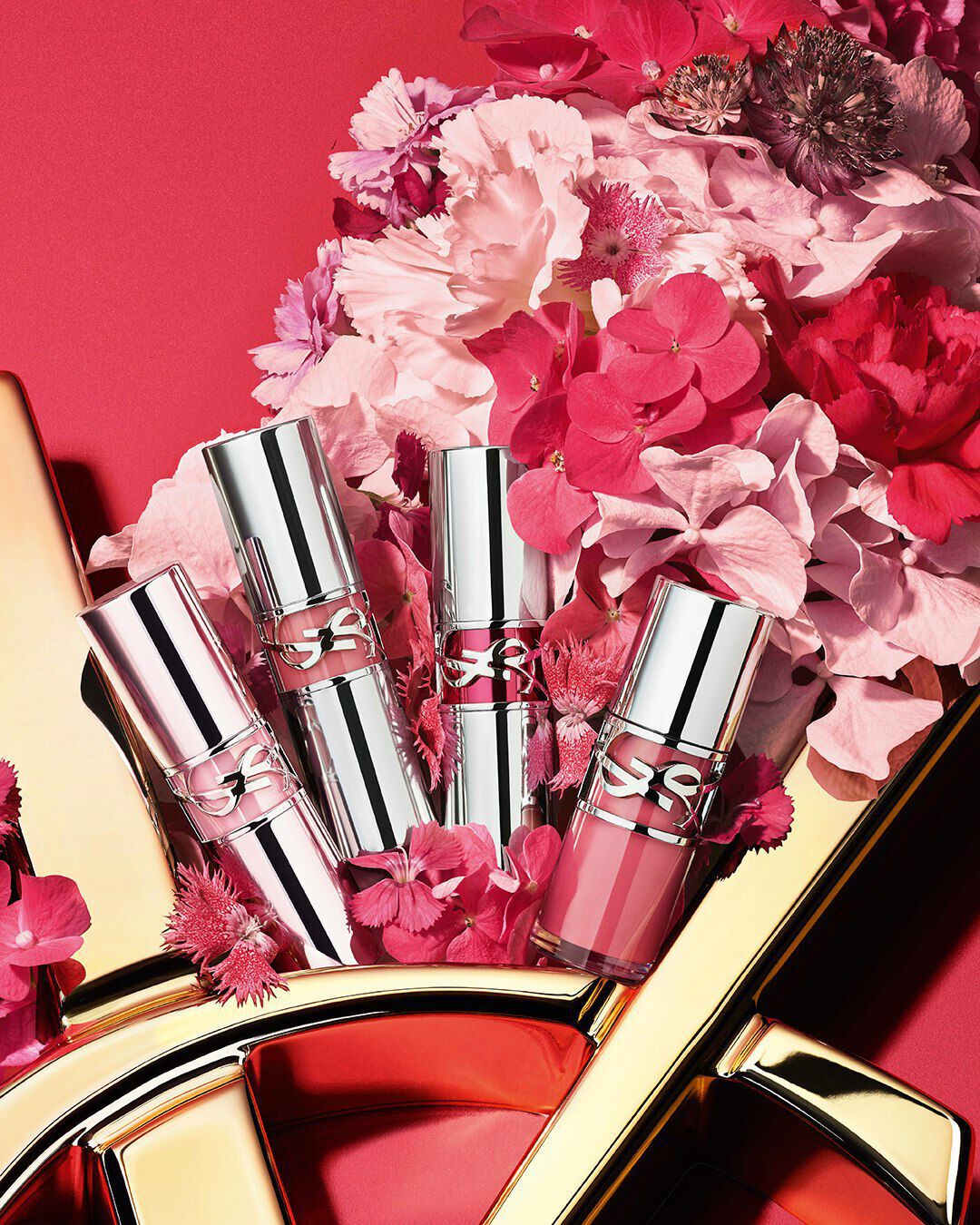 YSL Loveshine collection on a glossy gold YSL logo, with vibrant pink flowers, against a pink background.