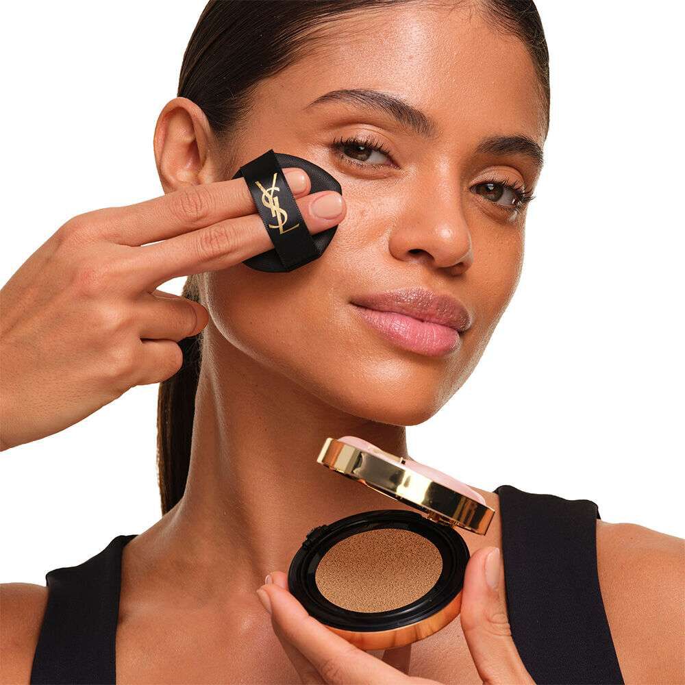Model with a smooth, radiant complexion holding the pink YSL SKIN AFFAIR CUSHION FOUNDATION to showcase a naturally glowing, flawless skin finish.
