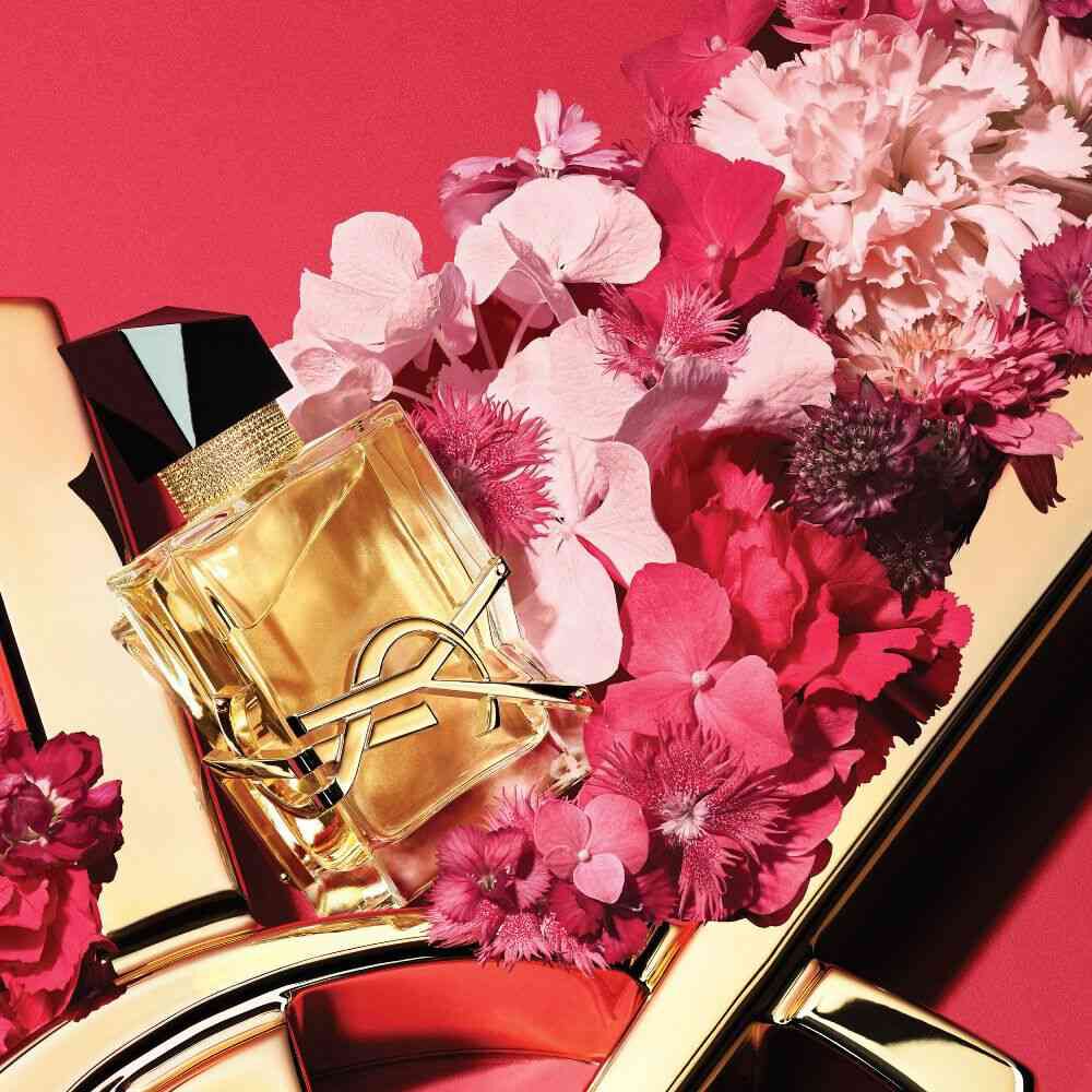 YSL Libre Eau de Parfum bottle with gold YSL logo, styled with pink and red flowers on a red background with a gold YSL logo detail.