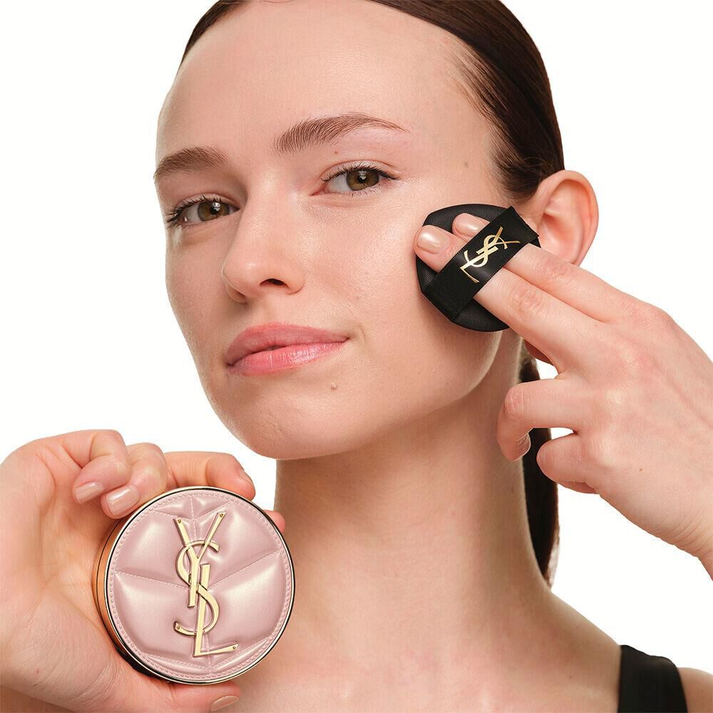 Model with a smooth, radiant complexion holding the pink YSL SKIN AFFAIR CUSHION FOUNDATION to showcase a naturally glowing, flawless skin finish.