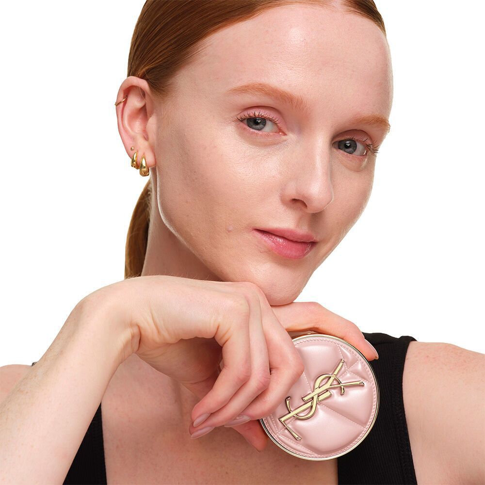 Model with a smooth, radiant complexion holding the pink YSL SKIN AFFAIR CUSHION FOUNDATION to showcase a naturally glowing, flawless skin finish.