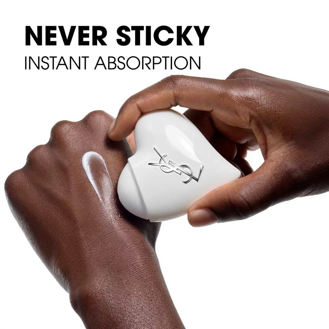 Dark-toned hands holding the Care Crush Hand & Body serum-in-cream white heart-shaped case and applying white cream.