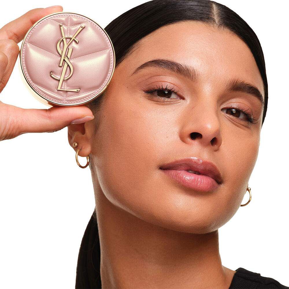 Model with a smooth, radiant complexion holding the pink YSL SKIN AFFAIR CUSHION FOUNDATION to showcase a naturally glowing, flawless skin finish.