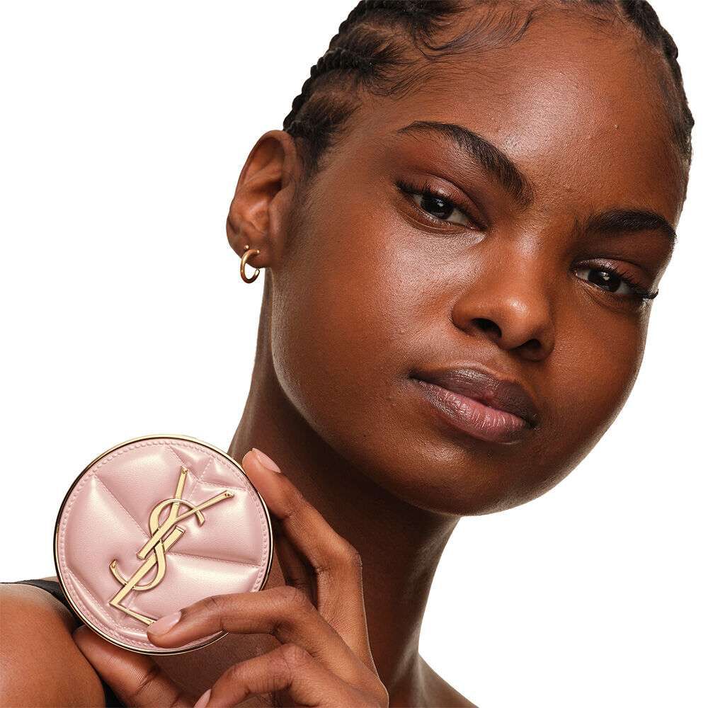 Model with a smooth, radiant complexion holding the pink YSL SKIN AFFAIR CUSHION FOUNDATION to showcase a naturally glowing, flawless skin finish.