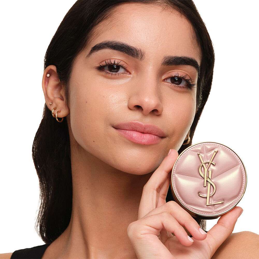 Model with a smooth, radiant complexion holding the pink YSL SKIN AFFAIR CUSHION FOUNDATION to showcase a naturally glowing, flawless skin finish.