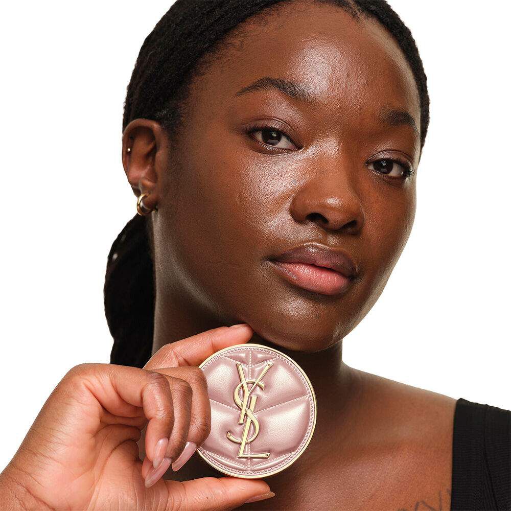 Model with a smooth, radiant complexion holding the pink YSL SKIN AFFAIR CUSHION FOUNDATION to showcase a naturally glowing, flawless skin finish.