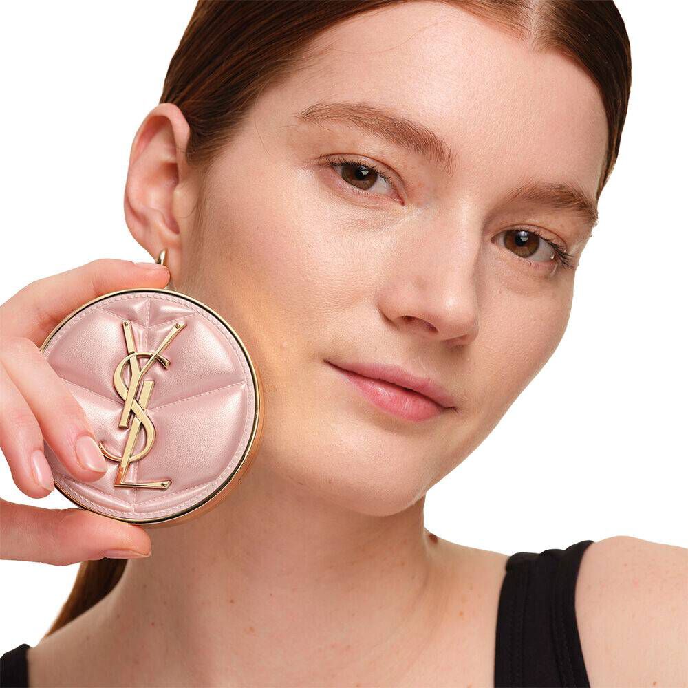 Model with a smooth, radiant complexion holding the pink YSL SKIN AFFAIR CUSHION FOUNDATION to showcase a naturally glowing, flawless skin finish.