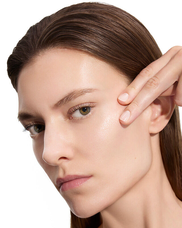 Marije, YSL Beauty model, with fair skin, gently touching her cheek, showcasing smooth skin after lotion application.