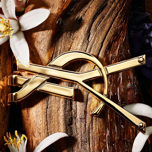 Golden YSL Cassandre lying on raw sandalwood bark with white orange blossoms.