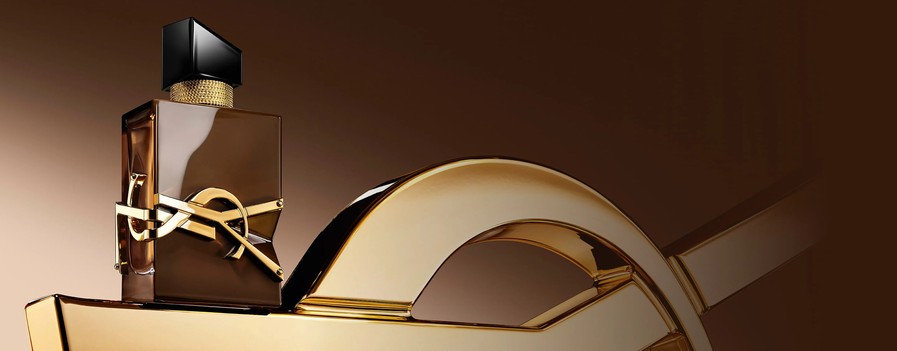 Glazed brown Libre Santal Couture bottle reflecting light, placed on a large golden YSL Cassandre.