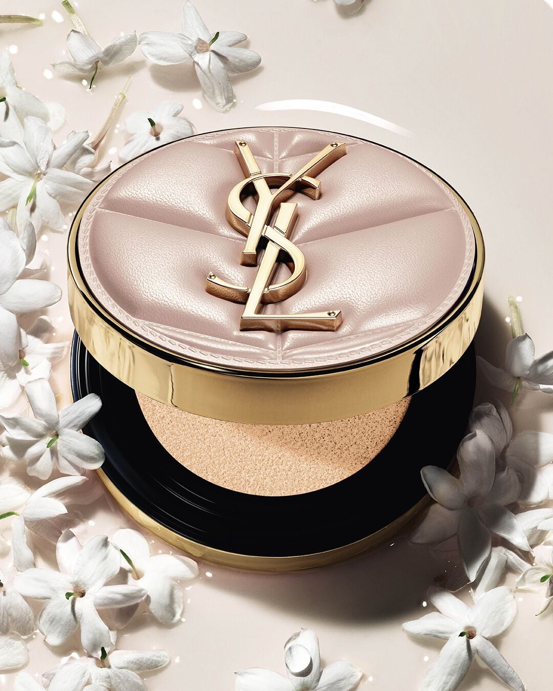Close-up of YSL SKIN AFFAIR SOFT GLOW CUSHION in a pool of liquid foundation and jasmine flowers. Radiant, sensorial finish.