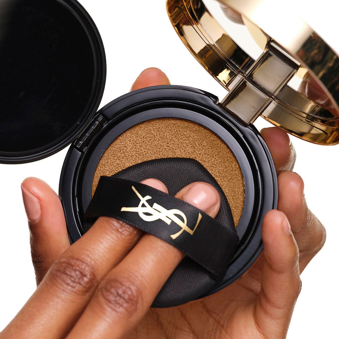 Loading the YSL SKIN AFFAIR SOFT GLOW CUSHION. Fingers under the black logo ribbon pressing the makeup puff.